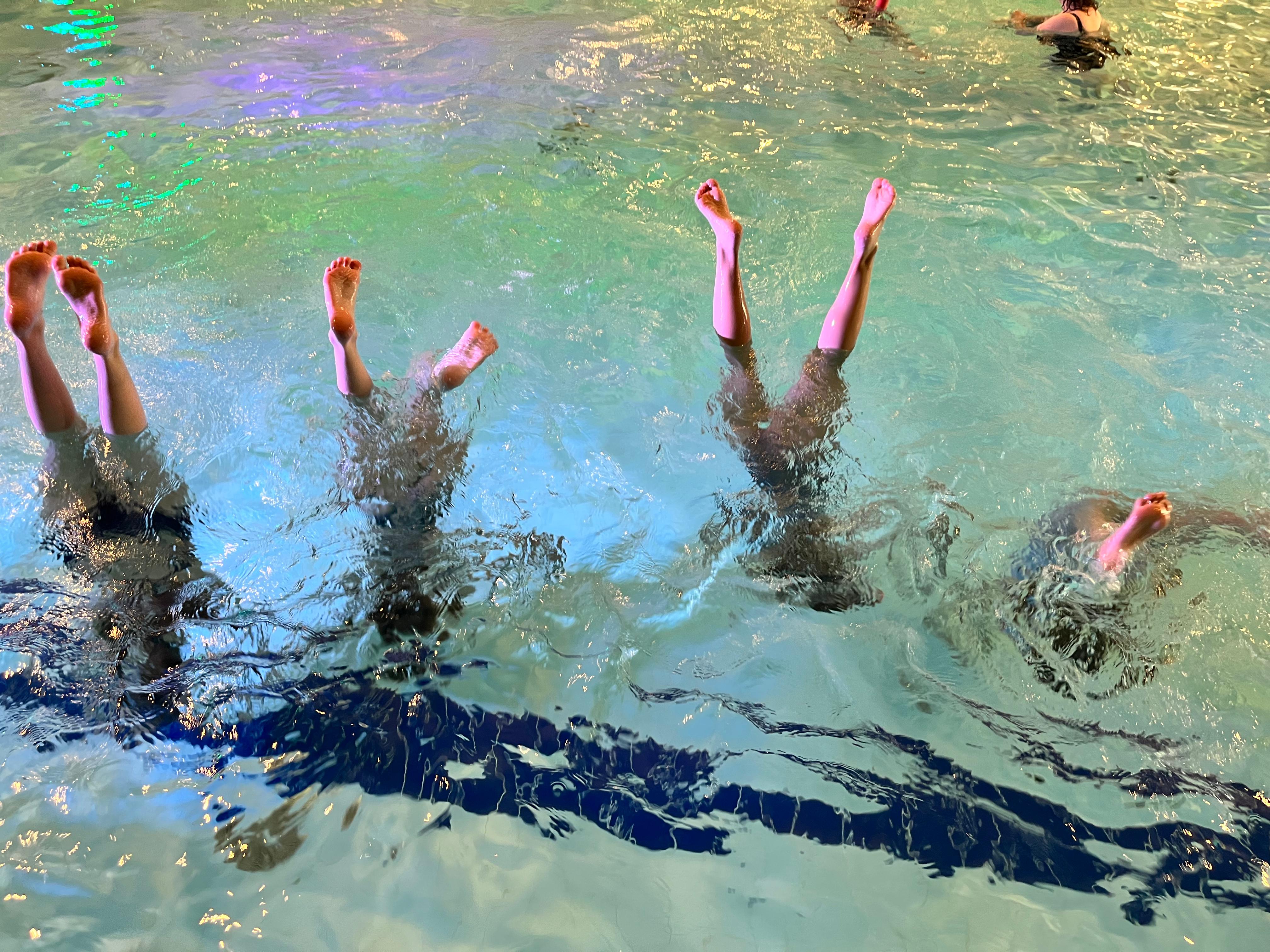 4 tyttöä seisoo käsillä uima-altaassa, varpaat pinnalla