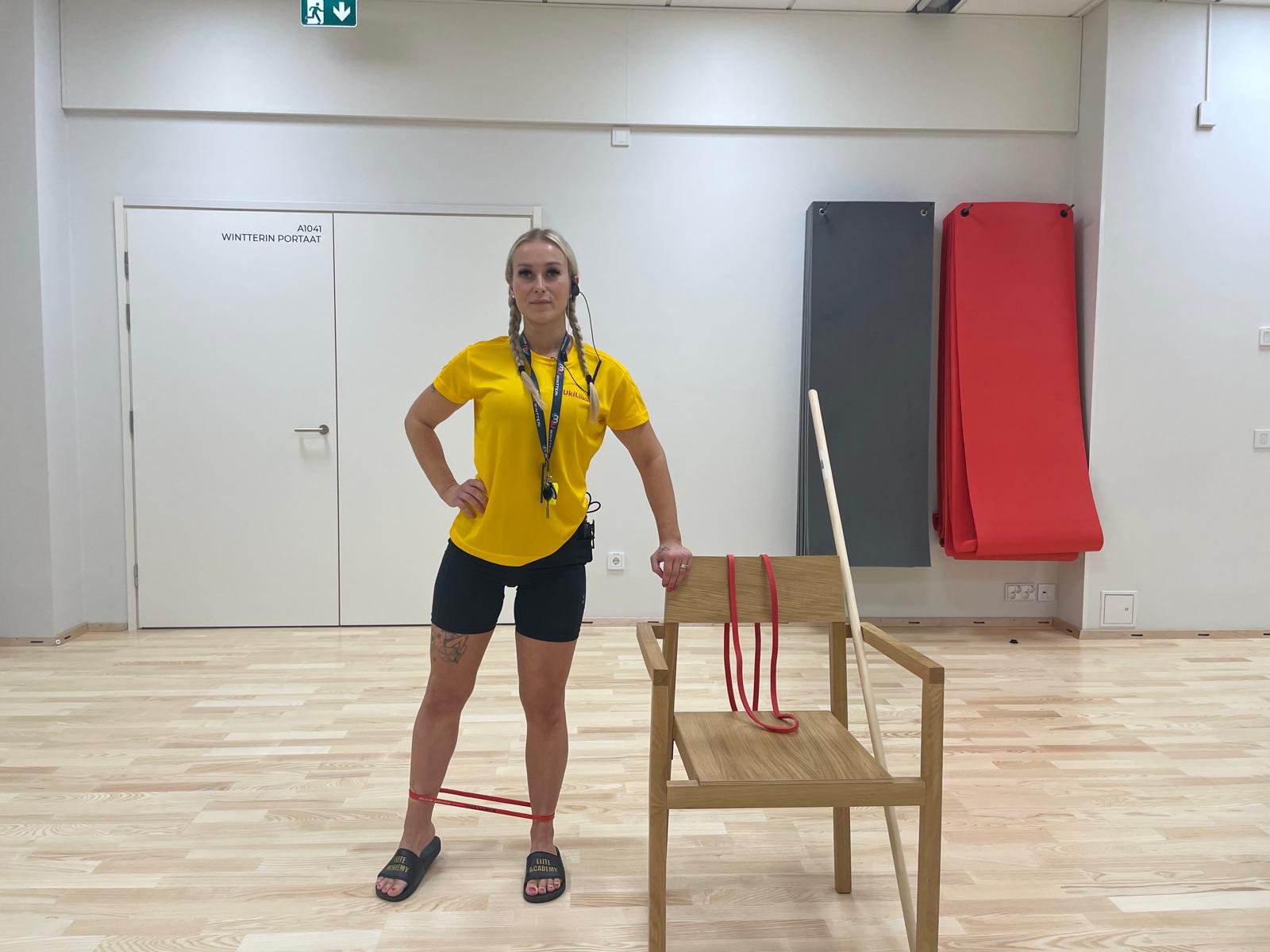 nainen ohjaa tasapainojumppa seisten, vierellä tuoli