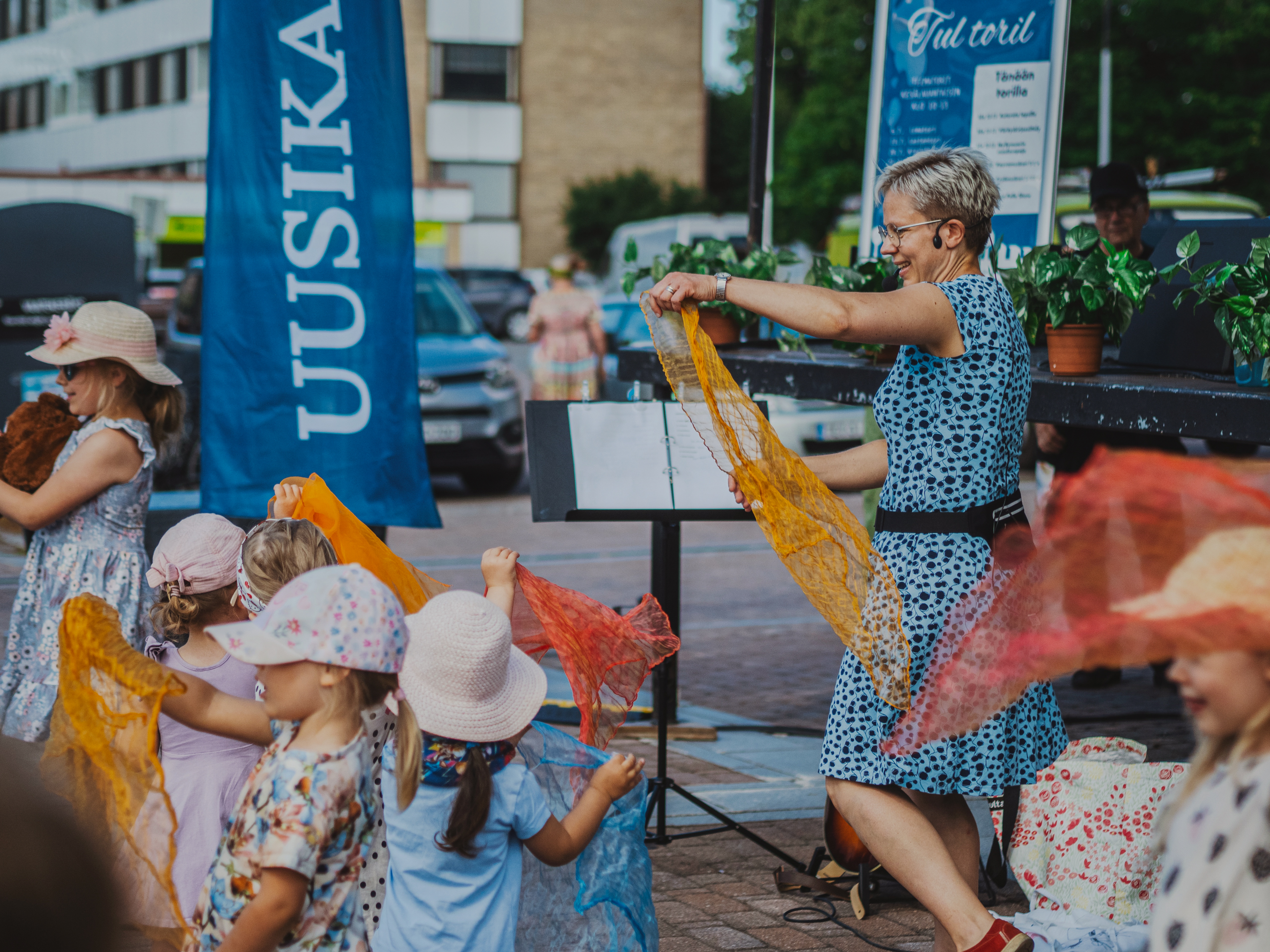 Lapset tanssivat torilla värikkäiden huivien kanssa.