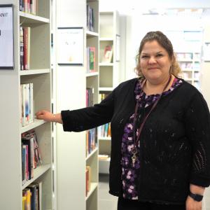 Kirjastotoimenjohtaja Salla Mäkinen katsoo hymyillen kameraan. Taustalla kirjaston hyllyjä.